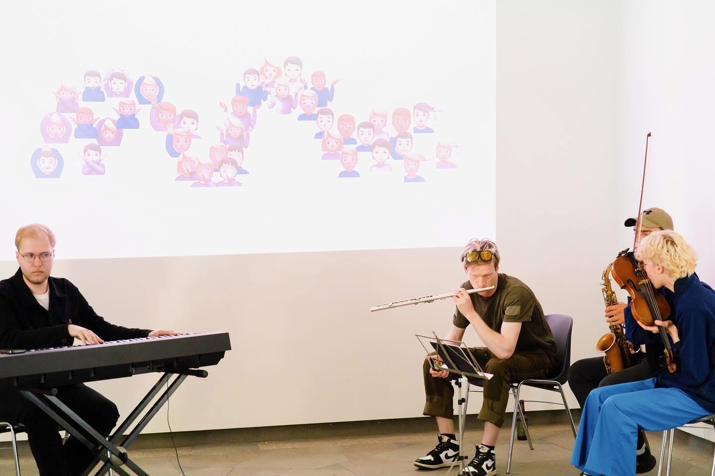 Musicians on keyboard, flute, saxophone and viola performing beneath a projected emoji score