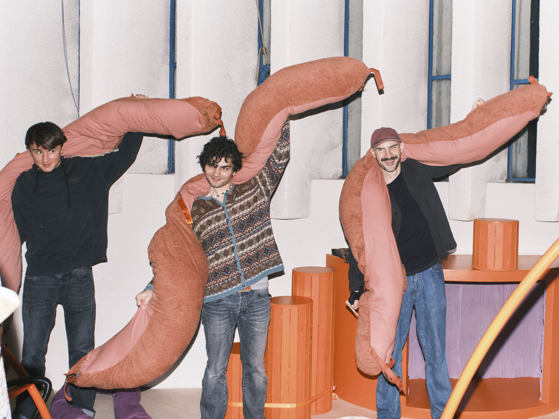 Three participants wearing plush soft-sculpture instruments between orange plinths at de Appel